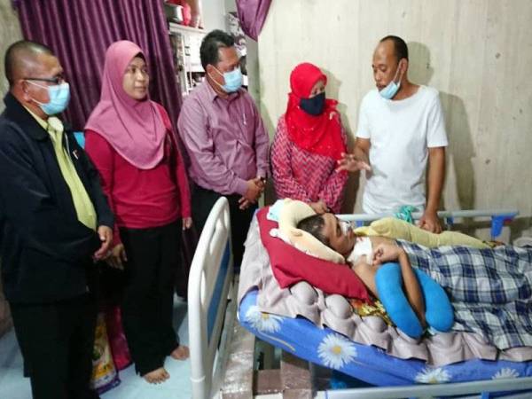 Zaiton (dua dari kanan) dan Arbain Ramli melihat Muhammad Israf yang terlantar akibat kemalangan di rumahnya di Taman Cahaya Masai, Pasir Gudang hari ịni.