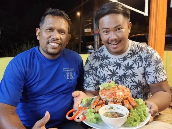 Mohd Lokeman (kiri) bersama pelanggannya menunjukkan hidangan ketam raja yang dijual di kedai makannya di Kampung Badang Jalan Pantai Cahaya Bulan.