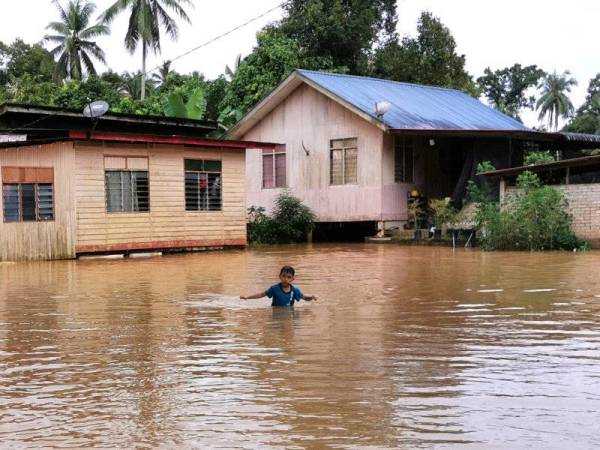 Seorang kanak-kanak berjalan di hadapan kediamannya yang dinaiki air di Kampung Kuala Ping, Setiu.