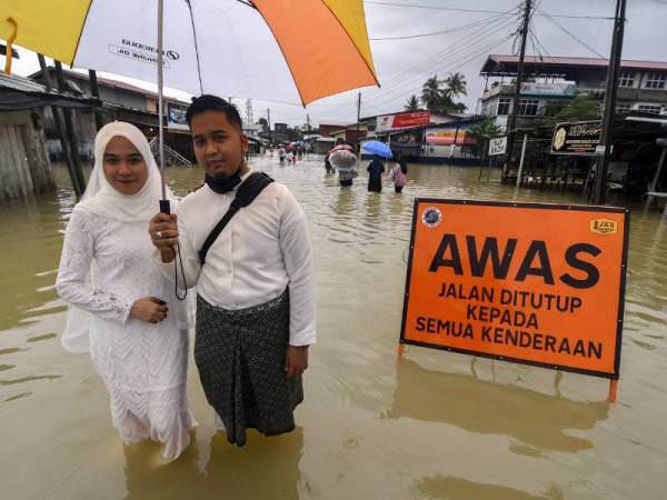 Pasangan pengantin Wan Muhammad Ridhwan Wan Yusoof dan Nor Aishah Ghazali terpaksa meredah banjir selepas selesai majlis akad nikah di Masjid Jubli Perak Sultan Ismail Petra atau lebih dikenali sebagai Masjid Beijing yang masih ditengelami banjir berikutan limpahan air Sungai Golok ketika tinjauan di Rantau Panjang hari ini. - Foto Bernama