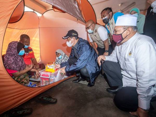 Perdana Menteri Tan Sri Muhyiddin Yassin (empat, kiri) menyampaikan sumbangan kepada mangsa banjir ketika melawat Pusat Pemindahan Sementara (PPS) Sekolah Kebangsaan Gual Tinggi pada Khamis. Turut hadir Menteri Besar Kelantan Datuk Ahmad Yakob (kanan). - Foto Bernama