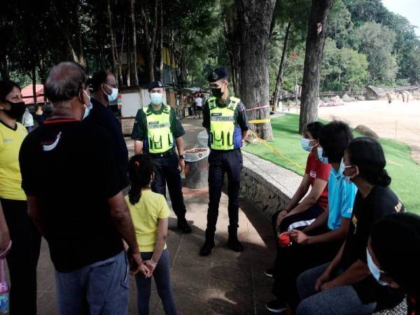 Dua anggota polis beramah mesra dan menasihati beberapa pengunjung agar mematuhi prosedur operasi standard (SOP) semasa mengunjungi Pantai Teluk Cempedak sempena cuti umum perayaan Krismas, hari ini. = Foto Bernama 