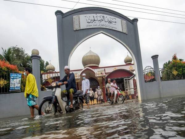 Beberapa jemaah yang selesai menunaikan solat Jumaat di Masjid Kampung Bendang Pa'yong di Tumpat pada Jumaat mengharungi limpahan air melebihi paras buku lali (kira-kira 0.3 meter) berikutan banjir termenung yang berlaku sejak Sabtu lepas. - Foto Bernama