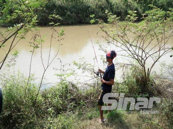 Terdapat penduduk menjalankan aktiviti memancing di Sungai Tumboh.