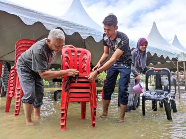 Mohd Idris (kiri) bersama anak dan menantunya membersihkan kerusi di depan rumahnya yang dinaiki air sejak malam Rabu.