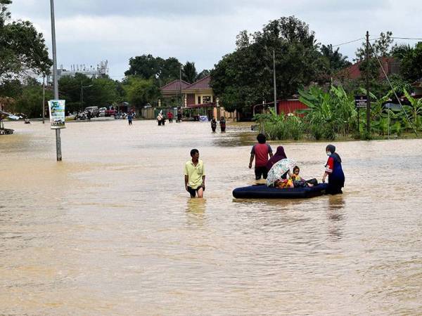 Seorang wanita membawa dua kanak-kanak meredah air banjir menggunakan tilam angin di Kampung Baru Bukit Mentok pada Jumaat - Foto Bernama