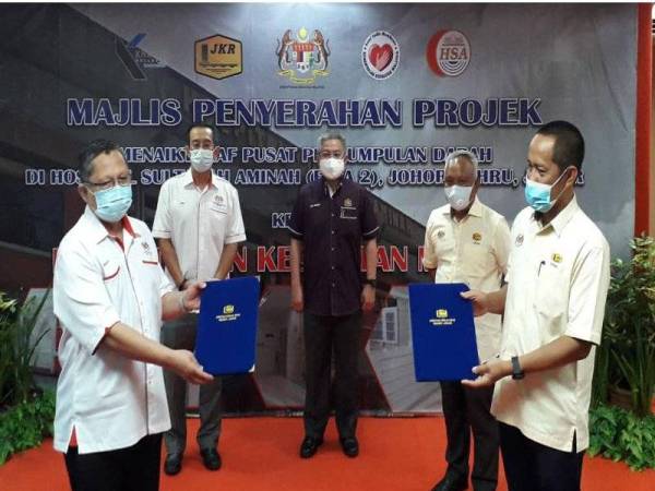 Dr Adham (tengah) menyaksikan pertukaran dokumen pada Majlis Penyerahan Projek Menaik Taraf Pusat Pengumpulan Darah di HSA, Johor Bahru pada Sabtu.