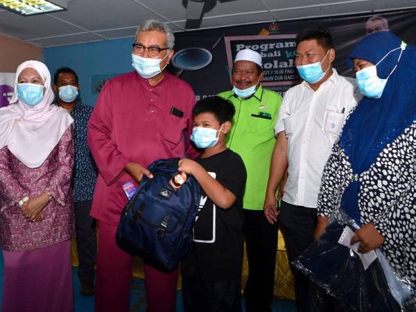 Mohd Redzuan (dua dari kiri) menyampaikan barangan persekolahan kepada Noor Hafizi Noor Azizul, 10, (tengah) pada Program Kembali ke Sekolah di Gadek, Alor Gajah, Melaka pada Sabtu. FOTO: BERNAMA