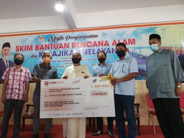 Syed Abu Hussin menyerahkan replika cek RM80,000 kepada Persatuan Nelayan Perak yang diwakili Pengerusinya, Mansor Yusof (dua dari kanan) pada majlis berkenaan di Bukit Gantang, Taiping pada Ahad.