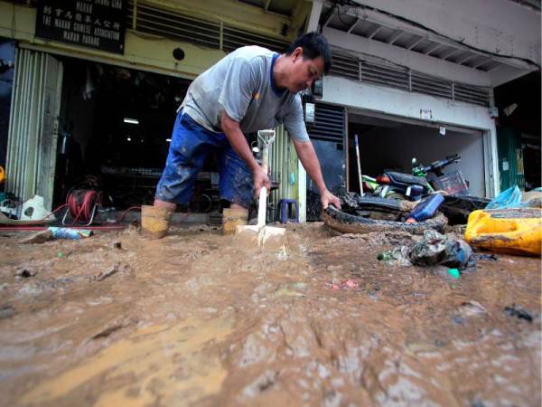 Pengusaha bengkel motosikal, Lai Kam Sung, 53, sibuk membersih kotoran dan lumpur di hadapan kedainya akibat banjir besar baru-baru ini semasa tinjauan Foto Bernama di Bandar Maran pada Ahad. - Foto Bernama