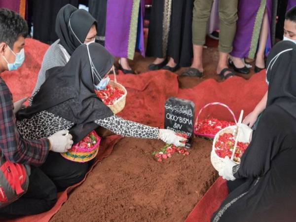 Aldha (dua dari kiri) menabur bunga di atas pusara suaminya ketika upacara pengebumian di Jakarta pada Khamis. - Foto AFP