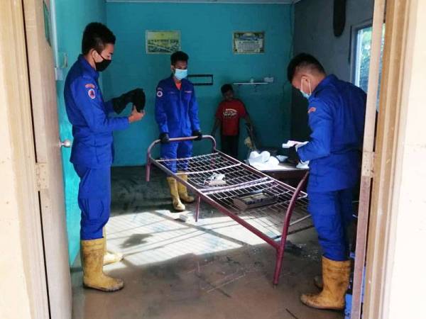 Anggota Angkatan Pertahanan Awam (APM) membantu mangsa banjir membersihkan kediaman mereka di Kampung Seremin, Segamat.