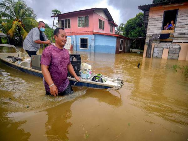 Penduduk kampung, Mohamad Fatihi,40, (depan) dibantu oleh rakannya kelihatan menggunakan sampan untuk memindahkan barang-barang elektrik ketika tinjauan di Kampung Rantau Panjang di Batu Kawa pada Rabu. - Foto Bernama