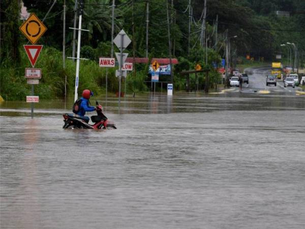 Seorang penunggang motosikal mengharung banjir yang menenggelamkan Jalan Kolupis Penampang hari ini. - Foto Bernama