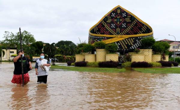 Penduduk di sekitar Pekan Donggongon Penampang melintasi jalan raya di bulatan Sigar yang ditenggelami banjir berikutan hujan lebat berterusan sejak semalam. -Foto Bernama