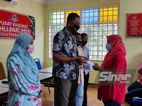 Rosol (tengah) menyampaikan bantuan kepada peniaga kecil dan penjaja yang terjejas banjir serta Covid-19 di Hulu Terengganu pada Isnin.