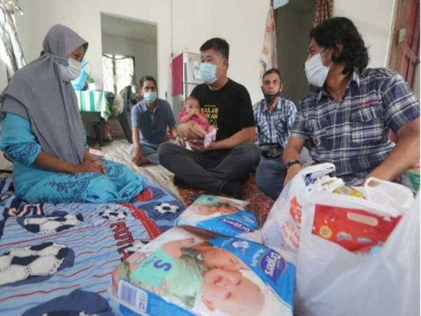 Chee Heng memangku Aisyah Naura Arumi ketika menyampaikan sumbangan kepada Mohd Khalil (kanan) dan Yeti Nasem (kiri) di rumah mereka di Kampung Bukit Belimbing, Kuala Selangor pada Selasa.