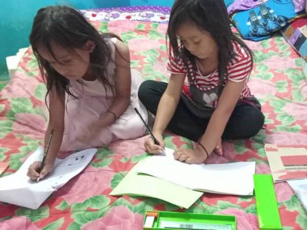 Nur Essya Qaisara, 7, (kanan) bersama kakaknya, Nur Elysia Natliyah, 9, belajar bersama-sama sementara menunggu giliran untuk belajar secara PdPR di rumah mereka di Kampung Suasa, Beaufort.