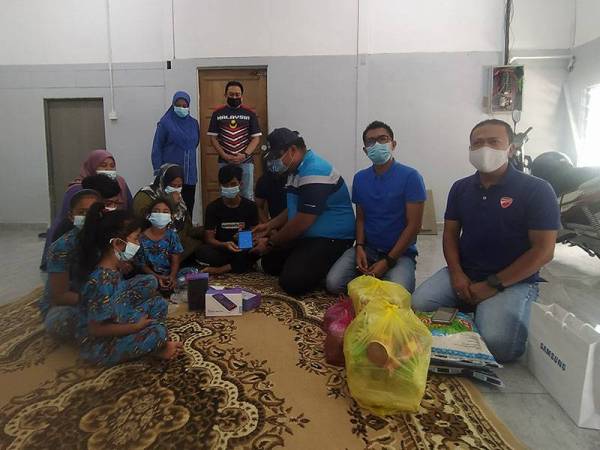 Syed Mohd Johan Rizal (tiga dari kiri) dan Mohd Fadzil (dua dari kiri) turun padang menyalurkan sumbangan tablet untuk kegunaan anak Saadiah Puteh (tengah) di Kampung Dewan, Alor Malai pada Sabtu.