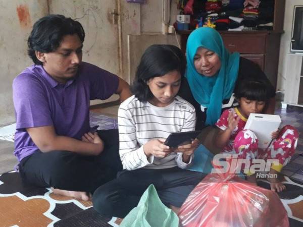 Nor Hazira (dua dari kiri) menunjukkan tablet yang diterimanya daripada YPM kepada Muhammad Hakim (kiri) dan Siti Hajah (dua dari kanan) di rumah mereka di Kampung Padang, Jalan Pegawai, Alor Setar pada Ahad.