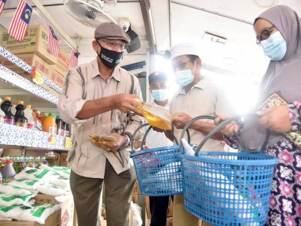 Rosol (kiri) membantu orang ramai yang datang membeli barang keperluan di Prihatin Mart di Kuala Telemong, Hulu Terengganu pada Isnin.