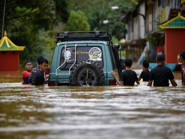 Penduduk Kampung Tebakang Dayak cuba mengalihkan kenderaan pacuan empat roda selepas Kampung itu dilanda banjir, Khamis. Foto Bernama