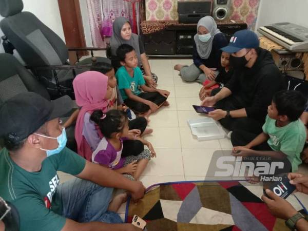 Onn Hafiz (kanan di tengah) menerangkan cara menggunakan tablet kepada anak-anak Mohd Afiq ketika menyerahkan sumbangan itu di Ladang Layang, pekan Layang-Layang, Kluang pada Isnin.