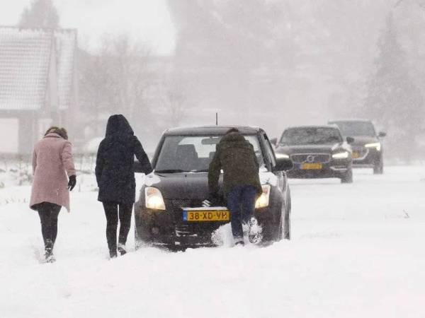 Tiga penduduk menolak sebuah kereta selepas ribut salji berlaku di Amsterdam pada Ahad. - AFP