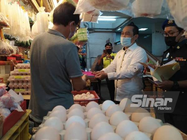 Abdul Yunus (tengah) menyerahkan tanda harga berwarna merah jambu kepada seorang peniaga telur ketika Sesi Walkabout dan pemantauan sempena Pelaksanaan Skim Harga Maksimum Musim Perayaan Tahun Baharu Cina 2021 di Pasar Besar Ipoh pada Selasa.