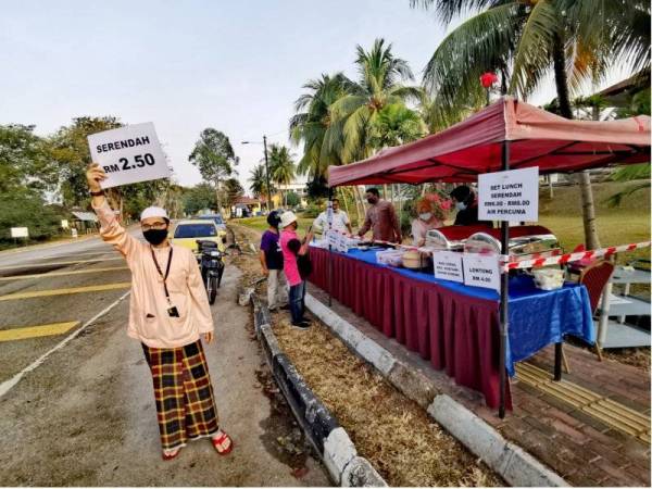 Shaharim memegang plakad bagi menarik orang ramai membeli makanan yang dihasilkan pihak hotel dan dijual di gerai tepi jalan di luar Hotel Seri Malaysia, Port Dickson pada Rabu.