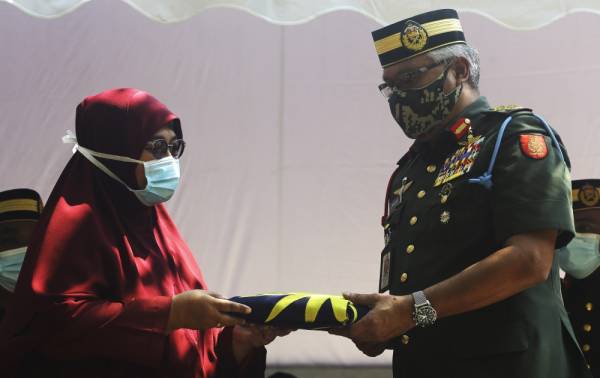 Zamrose (kanan) menyerahkan Jalur Gemilang kepada waris yang merupakan cucu saudara Allahyarham Veteran Perang Dunia Kedua Prebet Ujang Mormin, 100, selepas selesai proses pengebumian jenazah di Pusara Rejimen Askar Melayu Diraja (RAMD), hari ini. -Foto Bernama