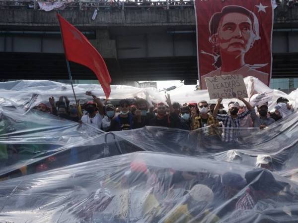 Kumpulan penunjuk perasaan antirampasan kuasa menggunakan plastik untuk melindungi diri mereka daripada semburan meriam air ketika menyertai protes di Yangon. - Foto AFP