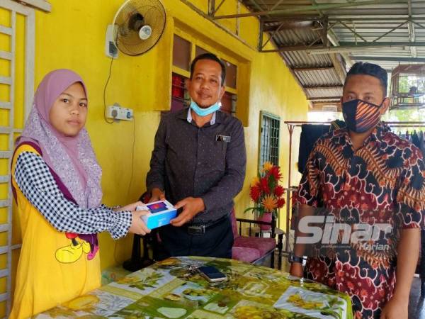 Zukri Suzita (tengah) bersama Ahmad Fadhli (kanan) menyampaikan sumbangan telefon pintar kepada Nur Hafizah di rumahnya di Kampung Bechah, Tendong, Pasir Mas.