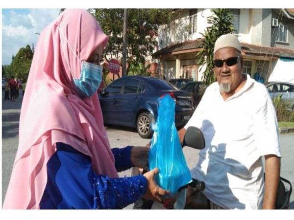 Norlida mengagihkan pek laksa secara pandu lalu di depan rumahnya di Taman Bukit Sentosa pada Sabtu