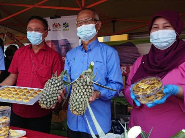 Ghazale (tengah) menunjukkan nanas morris Johor yang dipasarkan di pasar tani Jasin pada Rabu.