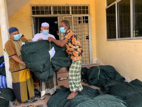 Dr Izani (tengah) menyampaikan pukat penternakan sangkar kepada salah seorang nelayan di Kampung Pulau Kundor pada Jumaat.