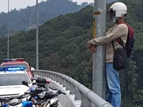 Lelaki yang menghadapi masalah rumah tangga itu berdiri di atas pembahagi jalan sambil berpaut pada tiang lampu. 