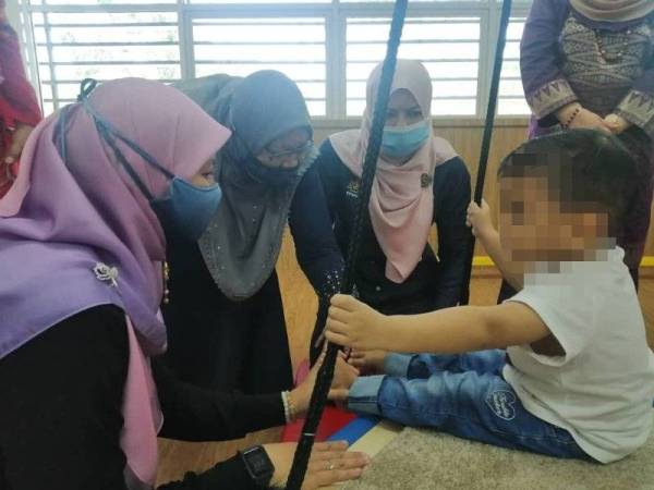 Rina (dua dari kanan) beramah mesra dengan seorang kanak-kanak lelaki OKU di Taska OKU Ikhlas, Pantai Peringgit di Melaka pada Sabtu.