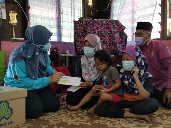 Noriah (kiri) menyampaikan faedah pengurusan jenazah berjumlah RM2,000 dan pencen penakat kepada Siti Rahayu setelah mendapati suaminya telah mencarum dengan Perkeso sehingga Januari lalu.