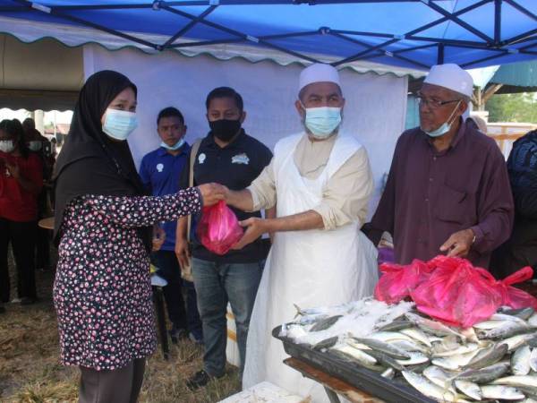 Syed Abu Hussin Hafiz memberikan dua kilogram ikan kembung kepada Normah Majid (kiri) sambil diperhatikan Pengerusi Persatuan Nelayan Kawasan Sungai Tinggi, Ahmad Abdullah (kanan) pada Program Ikan Rakyat bersempena program Kedai Bergerak Bukit Gantang Prihatin di tapak pasar malam Sungai Kerang, Trong pada Khamis. - Foto Bernama