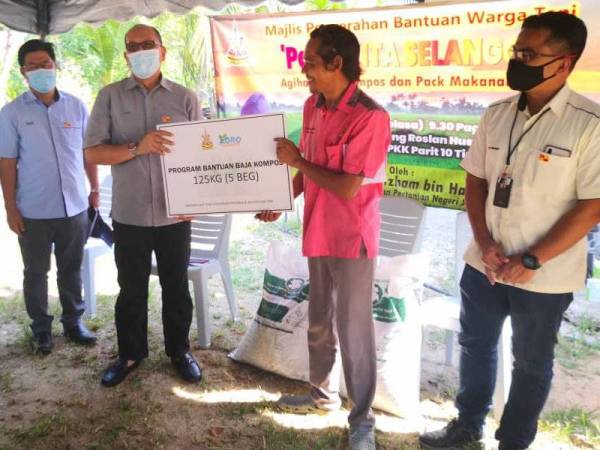 Izham (dua dari kanan) menyampaikan sumbangan bantuan baja kompos kepada salah seorang penerima pada Majlis Penyerahan Bantuan Warga Tani di Parit 10 Timur di sini pada Selasa.