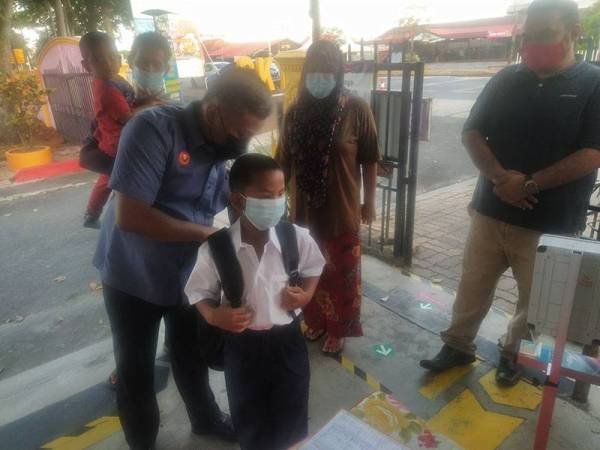 Yang Dipertua GPMS Cawangan Kuala Kedah, Amirul Syahir Musa (dua kiri) membantu Mohammad Danish sambil diperhatikan ibu bapanya ketika menghantar kanak-kanak itu ke sekolah buat kali pertama di SK Telok Kechai pada Isnin.