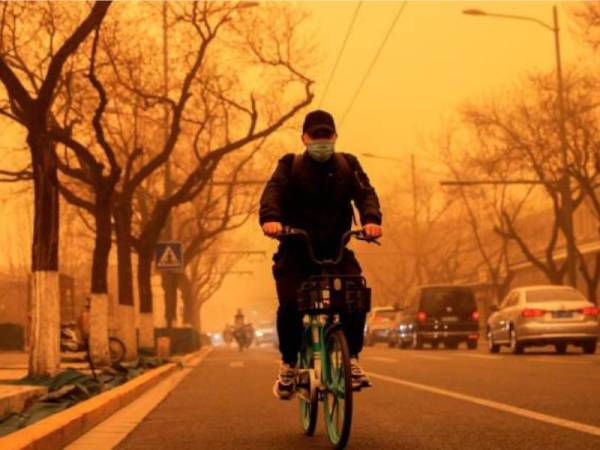 Penunggang basikal melalui kawasan yang dilanda ribut pasir pada waktu pagi di Beijing, China. - Foto Reuters