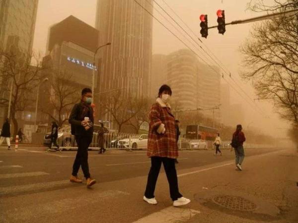 Beberapa orang yang memakai pelitup muka berjalan ketika Beijing dilanda jerebu kuning pada hari Isnin. - Foto AFP