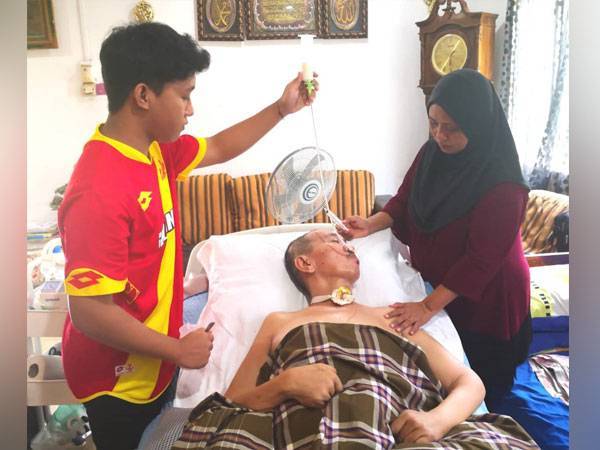 Muhammad Aiman memberikan minuman khas kepada Radzali menggunakan tiub melalui hidung sambil diperhatikan Siti Arbi semasa ditemui di rumah mereka di Kampung Bukit Cherakah pada Jumaat.