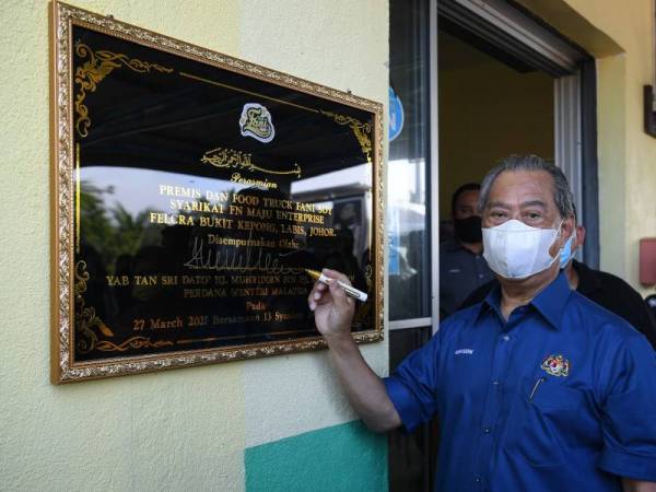 Muhyiddin menurunkan tandatangannya ketika merasmikan premis dan food truck Fani Soy, milik sebuah syarikat IKS bumiputera berasaskan produk kacang soya di Felcra Bukit Kepong, Labis hari ini. - Foto Bernama