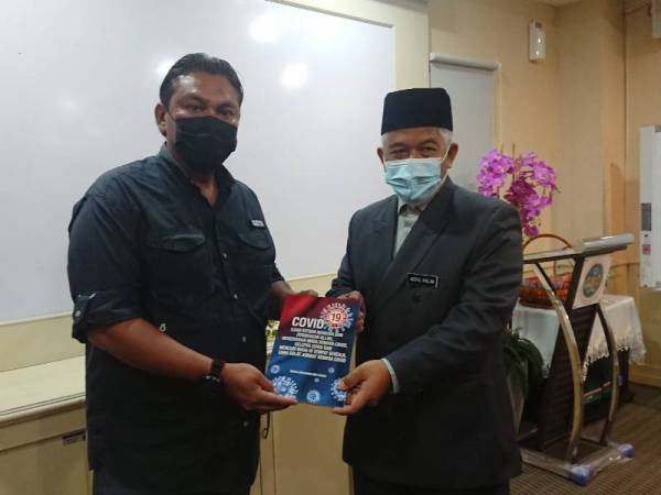 Halim (kanan) menyampaikan buku Covid-19 Melanda Negara dan Dunia kepada salah seorang pengamal media di Pejabat Jabatan Mufti Melaka di Bukit Palah pada Selasa.