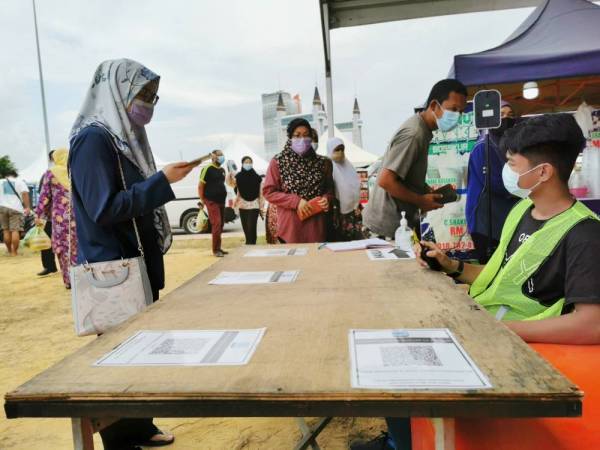 Pengunjung membuat imbasan suhu badan, kod QR melalui aplikasi MySejahtera dan menulis buku rekod kehadiran sebelum memasuki bazar Ramadan di dataran Jambatan Angkat, Kuala Terengganu pada Rabu.