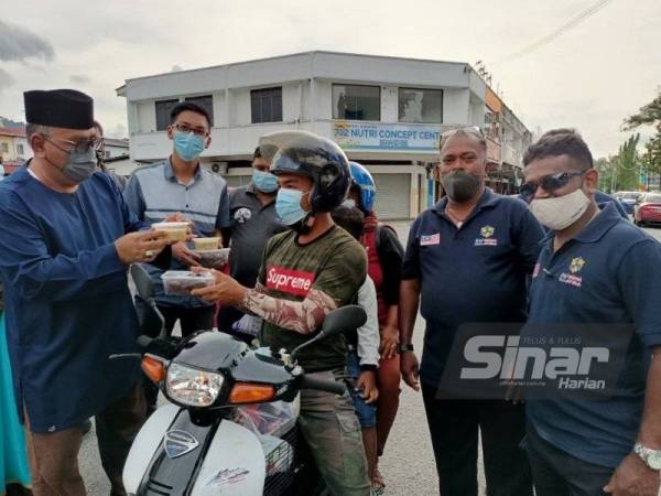 Mohd Zolkafly (kiri) mengangihkan bubur lambuk dan kurma kepada penduduk di sekitar tapak Pasar Malam Kampung Muhibbah, Sungai Siput pada Sabtu.