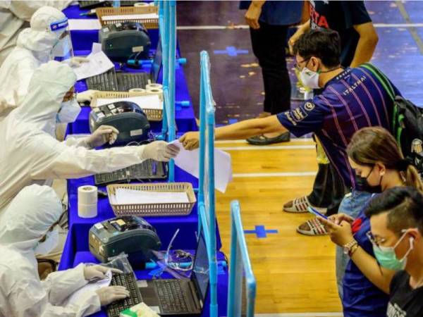 Pekerja perubatan yang memakai peralatan pelindung diri mendaftarkan orang di sebuah kompleks sukan di Bangkok pada Sabtu. - Foto AFP